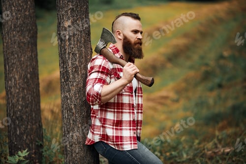 Preview: bearded lumberjack worker standing in forest with axe