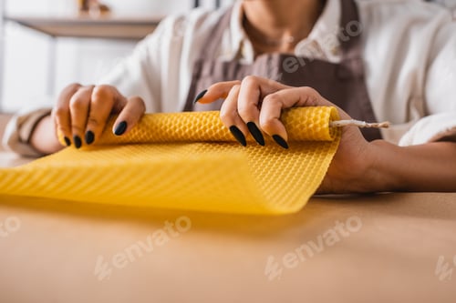 Preview: partial view of blurred african american woman making candle and rolling wax sheet in craft workshop
