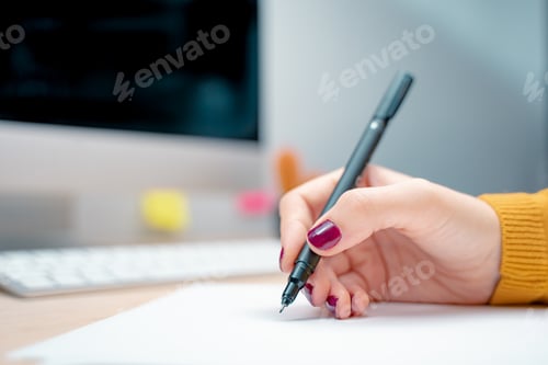 Preview: Beautiful female hand with manicure writing on a white paper at the office