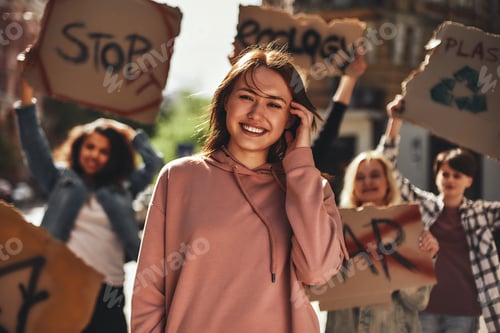 Preview: Save your planet. Young woman smiling and feeling happy while protesting for ecology with group of