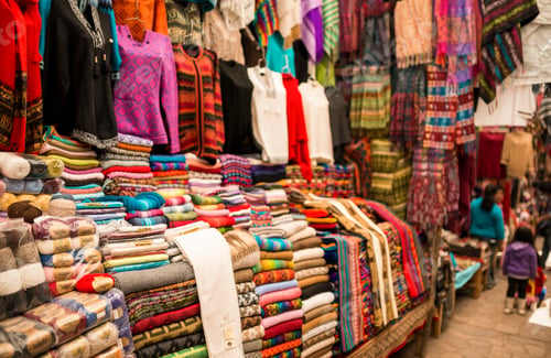 Preview: Colorful textile stall with shoppers browsing in a vibrant market atmosphere.