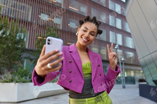 Preview: Attractive girl in fashionable outfit creats influence content shows peace sign at smartphone front