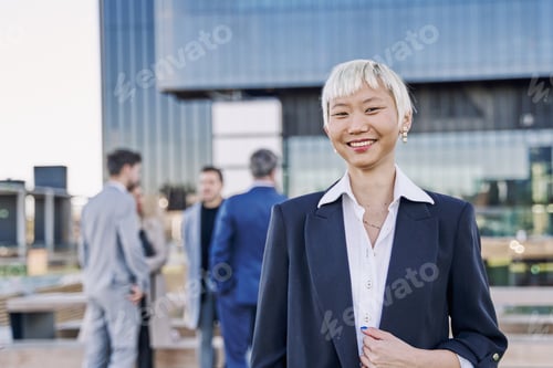 Preview: Portrait of a young Asian businesswoman smiling while her team is talking in the background.