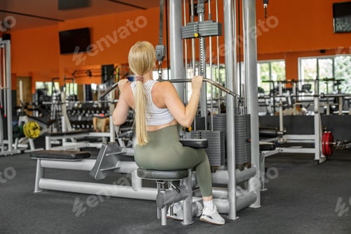 Preview: Woman exercising on lat pulldown machine in gym