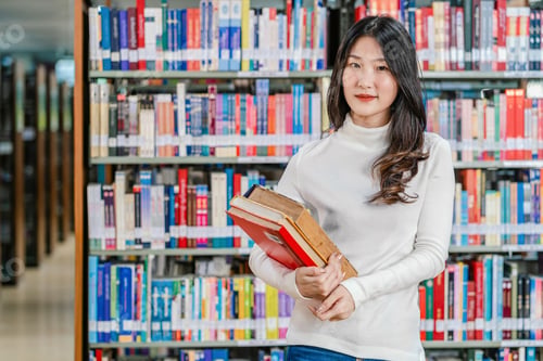 Preview: Portrait Asian young Student in casual suit standing and holding the book at book shelf