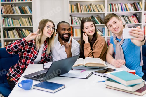 Preview: Happy young university students making selfie photo togethr while studying in library. Group of