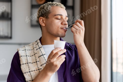 Preview: Young man enjoying a healthy yogurt snack for breakfast, closing eyes with pleasure