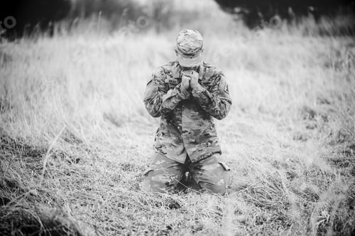 Preview: Grayscale shot of an American soldier praying in a field while kneeling on a dry grass