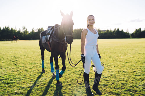 Preview: Cheerful horsewoman walking on field with horse