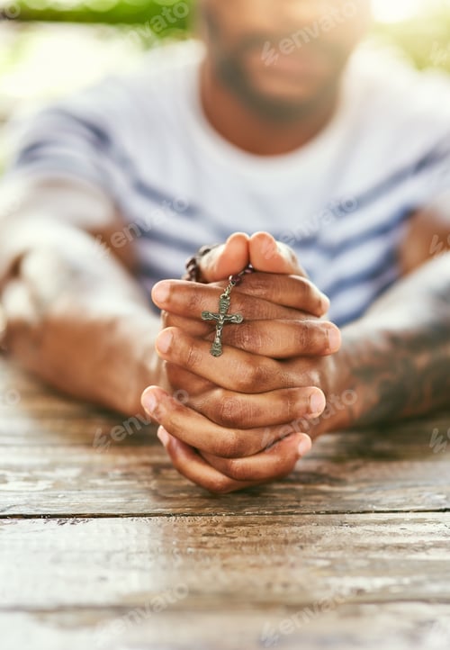 Preview: True to his religion. Cropped shot of a young man holding his rosary while praying.