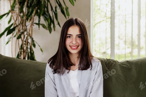 Preview: Beautiful smiling caucasian girl sitting at green sofa and watching at camera