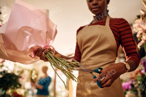 Preview: Black florist cutting flowers while making bouquet at flower shop.