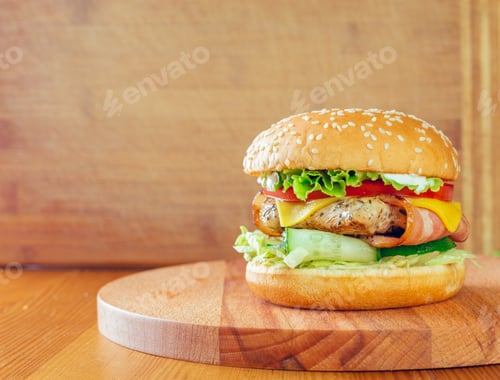 Preview: Juicy grilled chicken burger with fresh toppings on a wooden cutting board