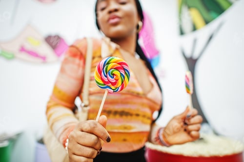Preview: African american millennial lady at candy shop with lolipops.