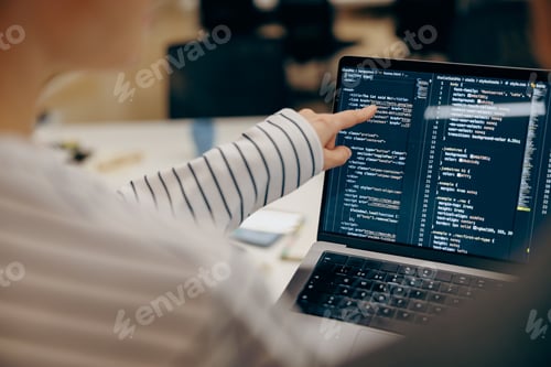Preview: Close up of female software engineer writing code on laptop with screens setup in coworking