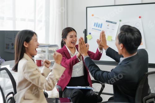 Preview: Business team celebrating success with high five in modern office.