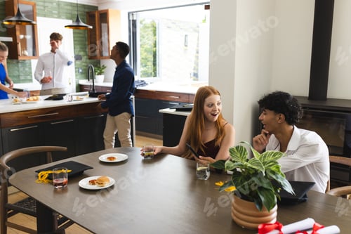 Preview: Teens enjoying casual gathering at home, chatting and laughing around dining table