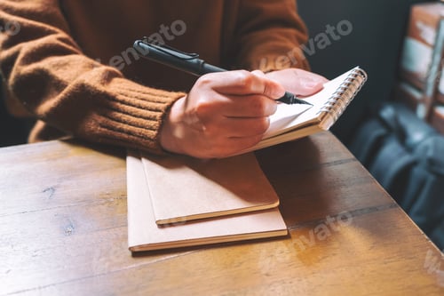 Preview: Closeup image of a woman holding and writing on blank notebook with fountain pen on wooden table