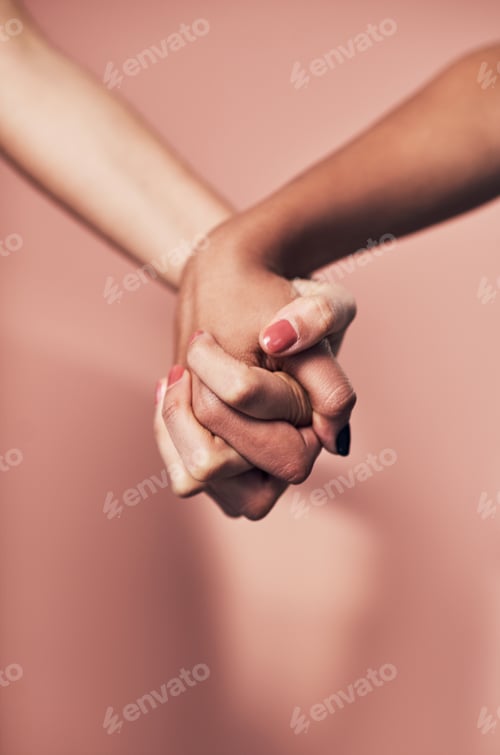 Preview: Shot of two unrecognizable women holding hands against a pink background