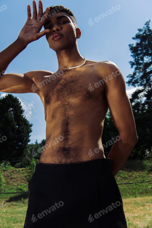 Preview: low angle view of african american man obscuring face with hand and looking at camera in park