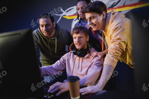 Preview: Cheerful multiethnic men looking at friend playing video game on computer in gaming club