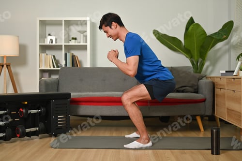 Preview: Muscular man in sportswear is doing squat exercises at home.