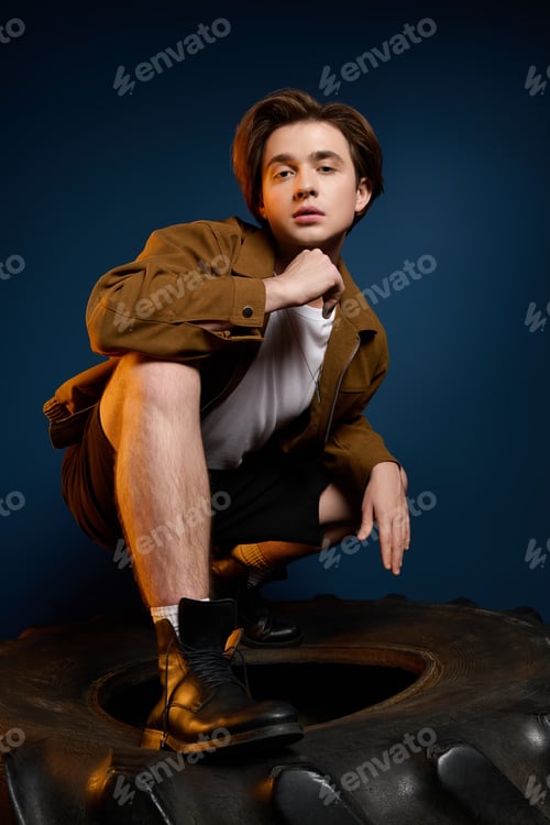 Preview: Young fashionable man showcasing stylish pose against a dark blue backdrop in a creative shoot