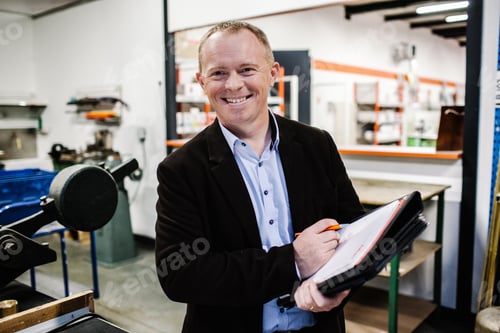 Preview: Man holding a catalog paperwork in a workshop smiling