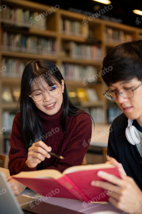 Preview: Glasses asian woman student pointing pencil in book man friend holding while sits at library's table