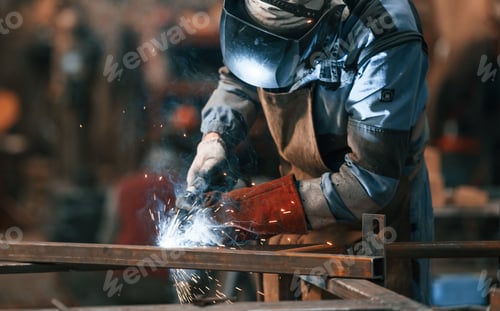 Preview: Close up view. Factory worker in protective mask is welding the iron