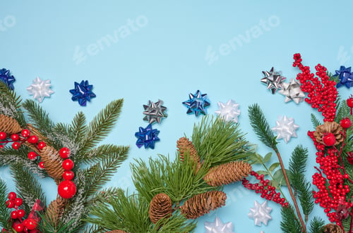 Preview: Decorative Christmas branch with red berries and pine cones on a blue background, top view