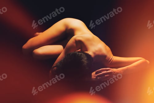 Preview: Unrecognizable female with naked body lying in black studio