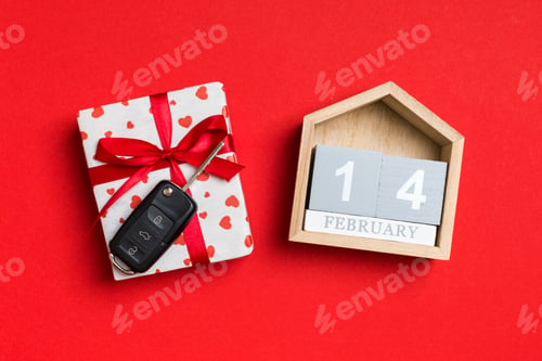Preview: Top view of car key on a gift box with red hearts and festive calendar