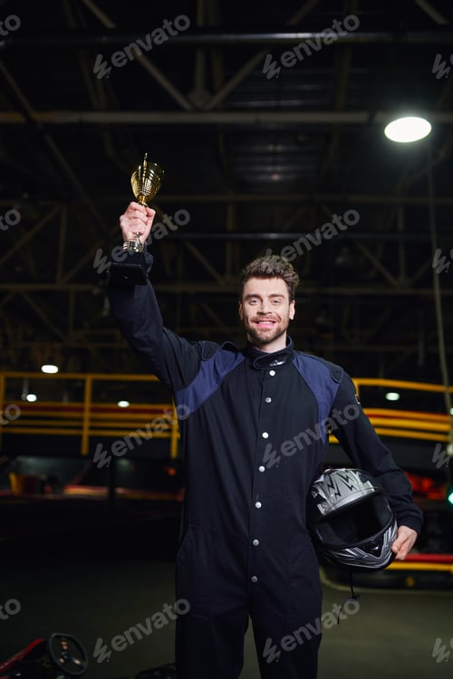 Preview: Smiling Man Holding Trophy and Helmet Indoors