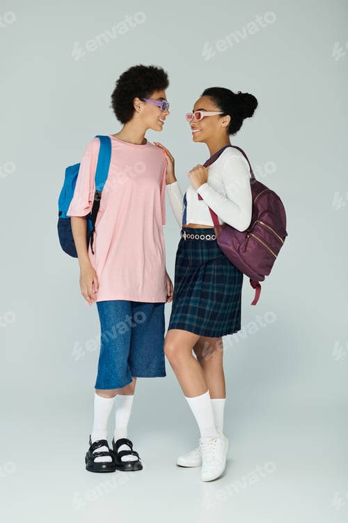 Preview: Two friends sharing a joyful moment in stylish outfits with backpacks against a light backdrop