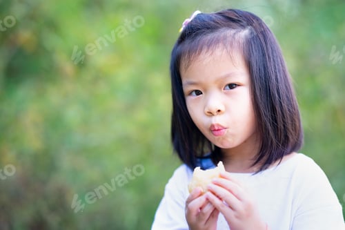 Preview: Portrait Asian kid girl bite fried bread. Child is hungry snack. Brunch time.