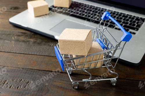 Preview: Composition of shopping cart with boxes and laptop on wooden background