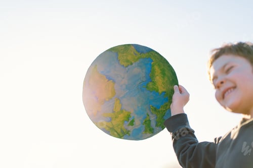 Preview: Little boy holding planet in hands against green spring background. Earth day