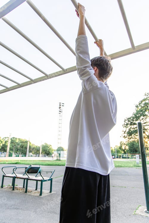 Preview: Young Man Doing Pull Ups on a Monkey Bar in a Park on a Sunny Day