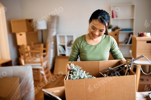 Preview: Happy Asian woman unpacking her belongings while relocation in new home.