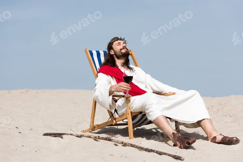 Preview: Jesus in robe and red sash resting on sun lounger with glass of red wine in desert