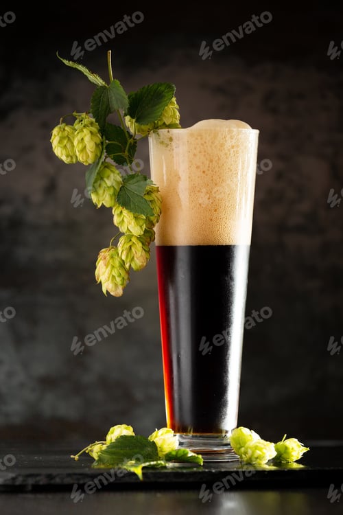 Preview: Glass of dark beer with hops around on a dark background