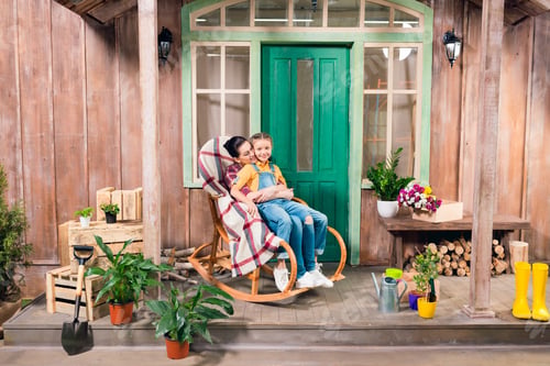 Preview: mother and daughter sitting in rocking chair and hugging on porch