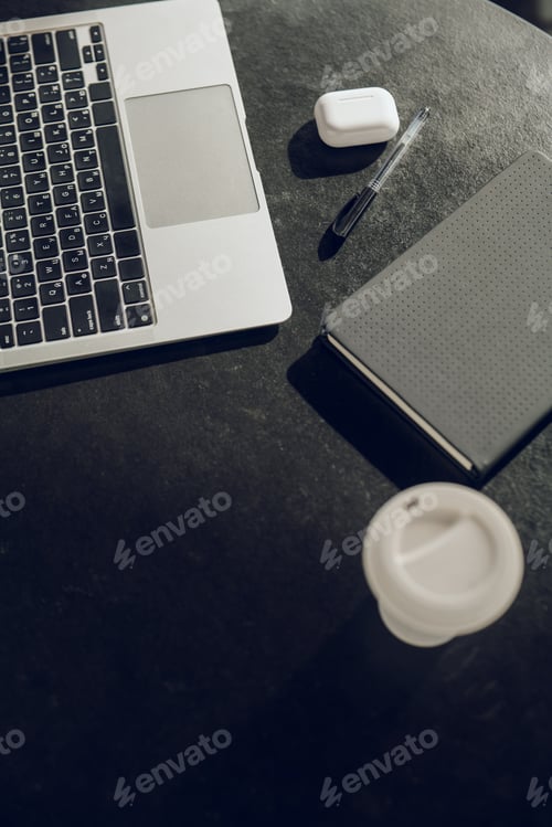 Preview: Laptop placed on black table near notebook and takeaway coffee