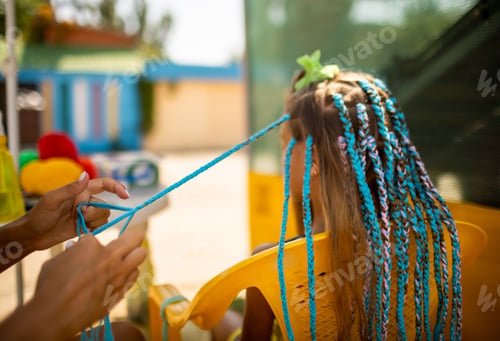 Preview: A girl in a suit weaves African braids in her hair on a sunny day