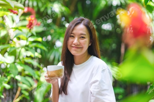 Preview: Portrait image of a young woman holding and drinking coffee in the garden