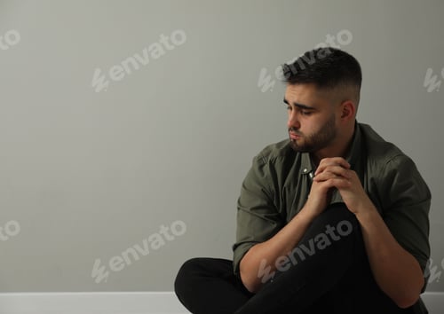 Preview: Sad man sitting near light grey wall. Space for text