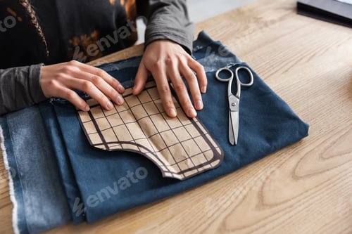 Preview: Cropped view of african american designer holding sewing pattern near cloth and scissors