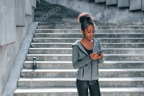Preview: Uses phone. Young african american woman in sportive clothes have workout outdoors at daytime