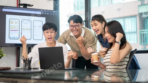 Preview: Asian man and coworkers raising fist in excited while looking at laptop on glass top table in office